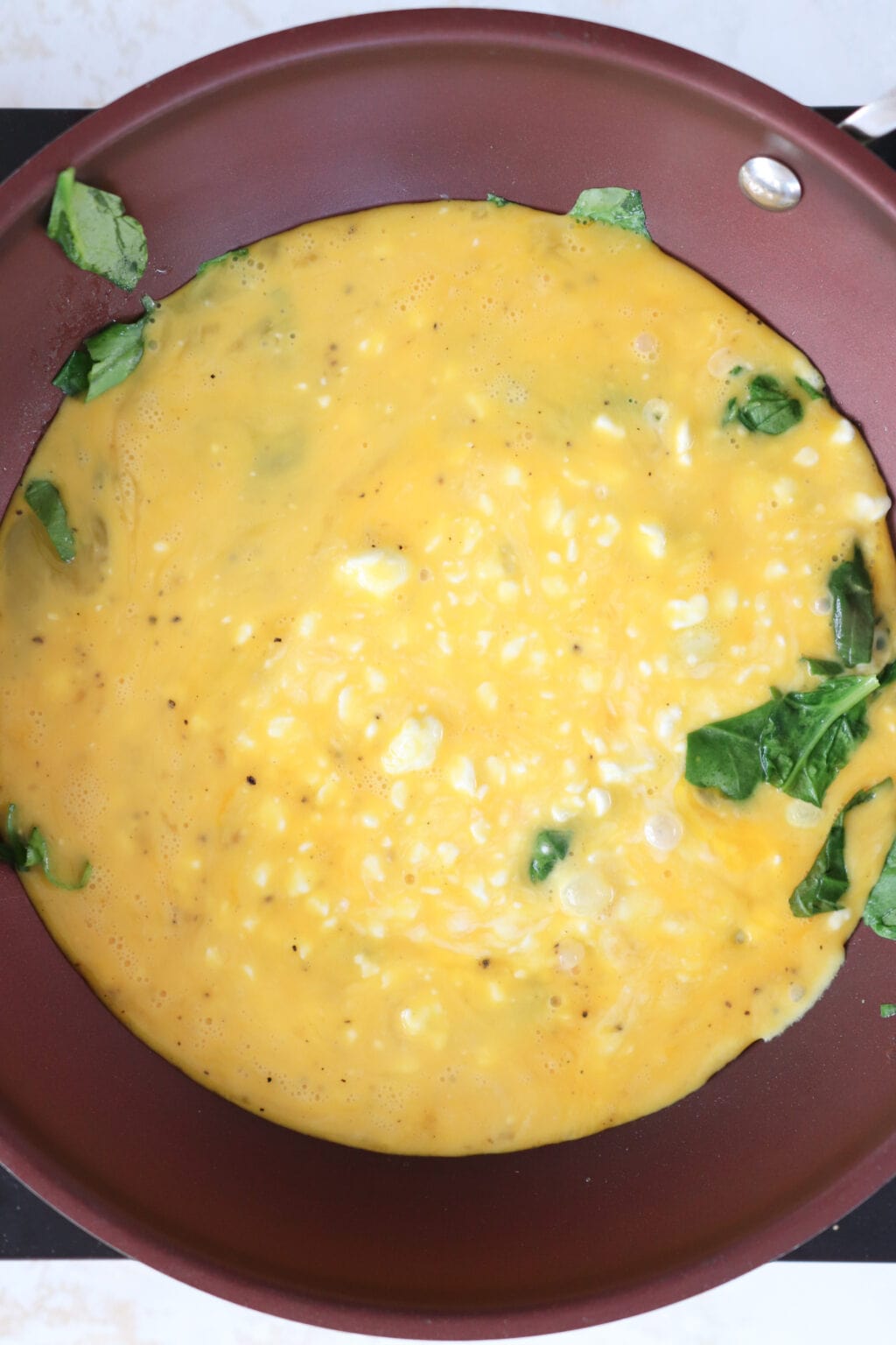 Uncooked scrambled eggs with spinach being cooked in a frying pan