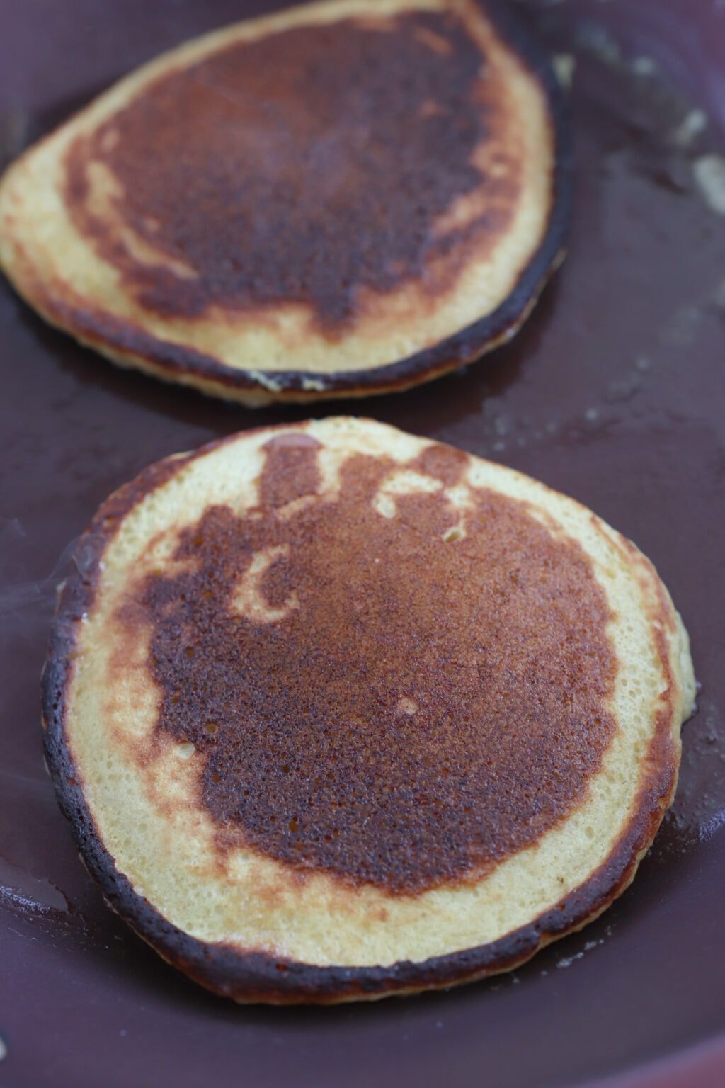 Two cooked golden brown pancakes in a frying pan.