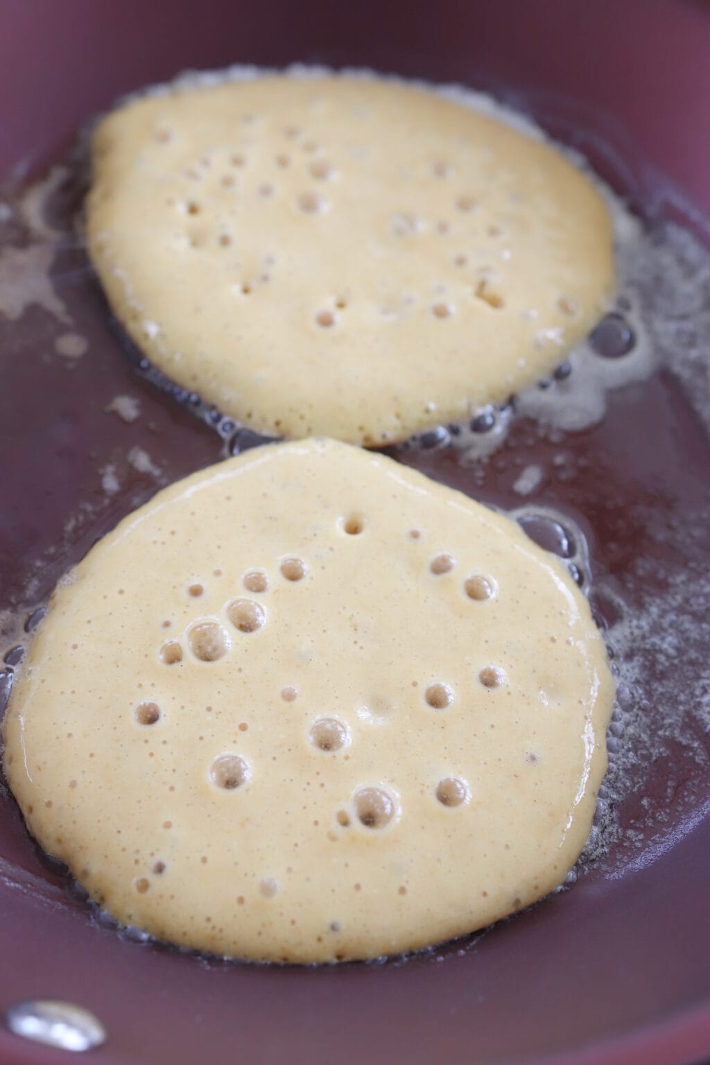 Two bubbling pancakes in a frying pan.