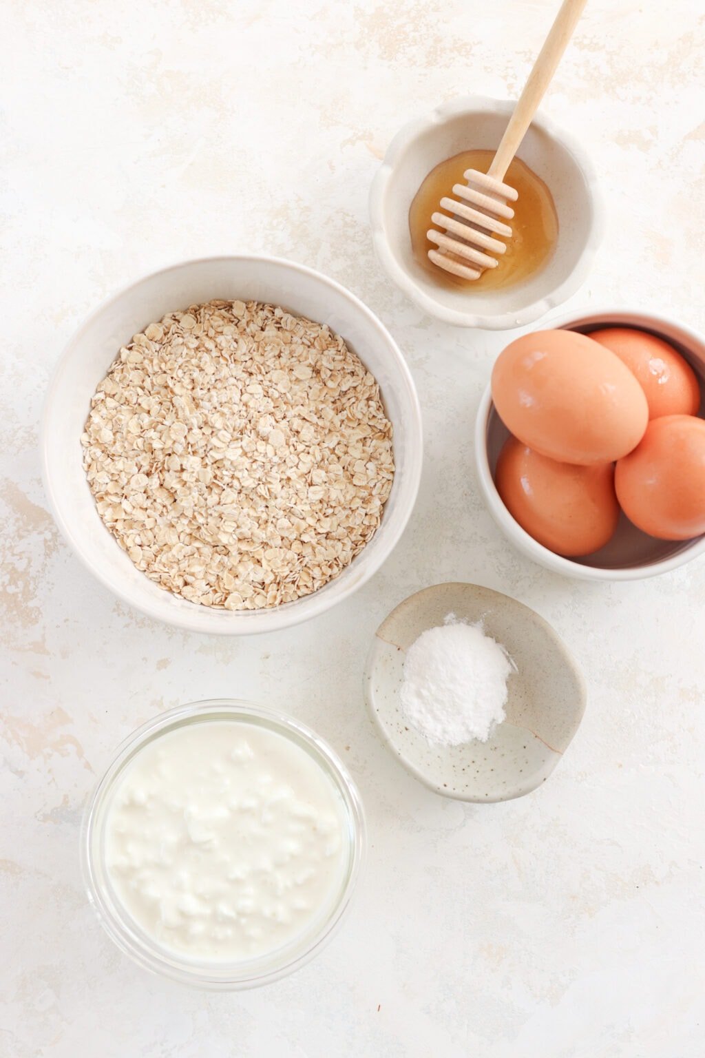 Ingredients for recipe in small bowls includes honey, quick oats, eggs, salt, and cottage cheese