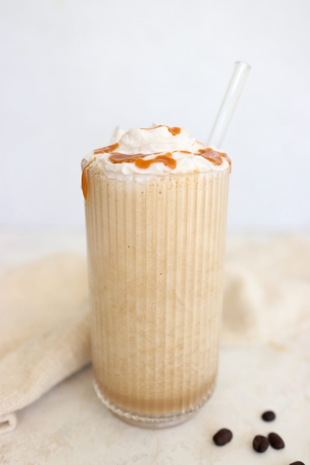 High protein coffee smoothie topped with whipped cream and caramel drizzle in a tall glass with a glass straw. 