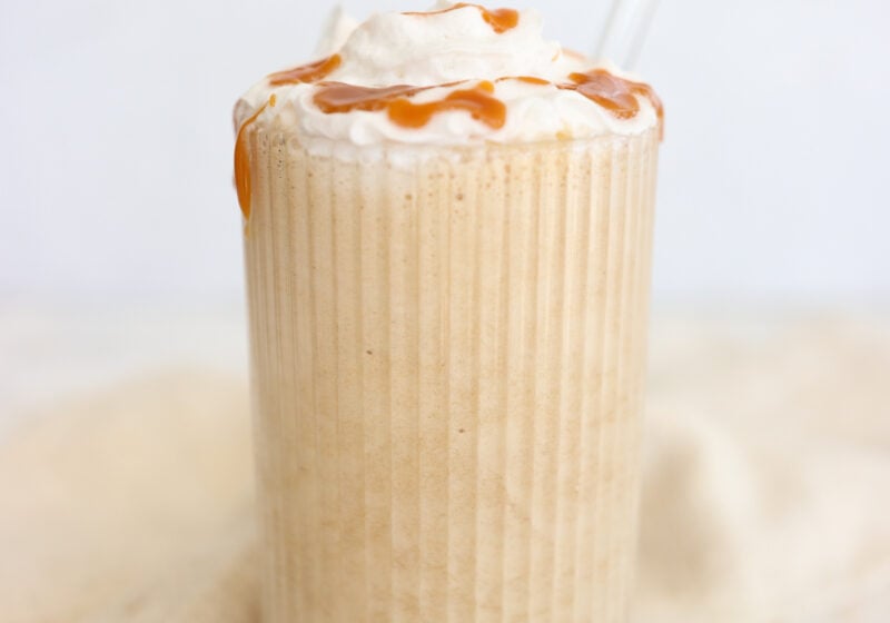 High protein coffee smoothie topped with whipped cream and caramel drizzle in a tall glass with a glass straw.