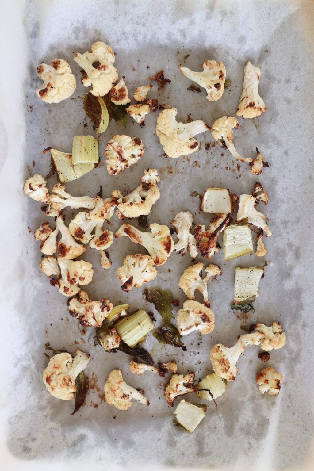 A baking sheet has roasted cauliflower on it. The cauliflower is a nice mix of white and golden brown in color.