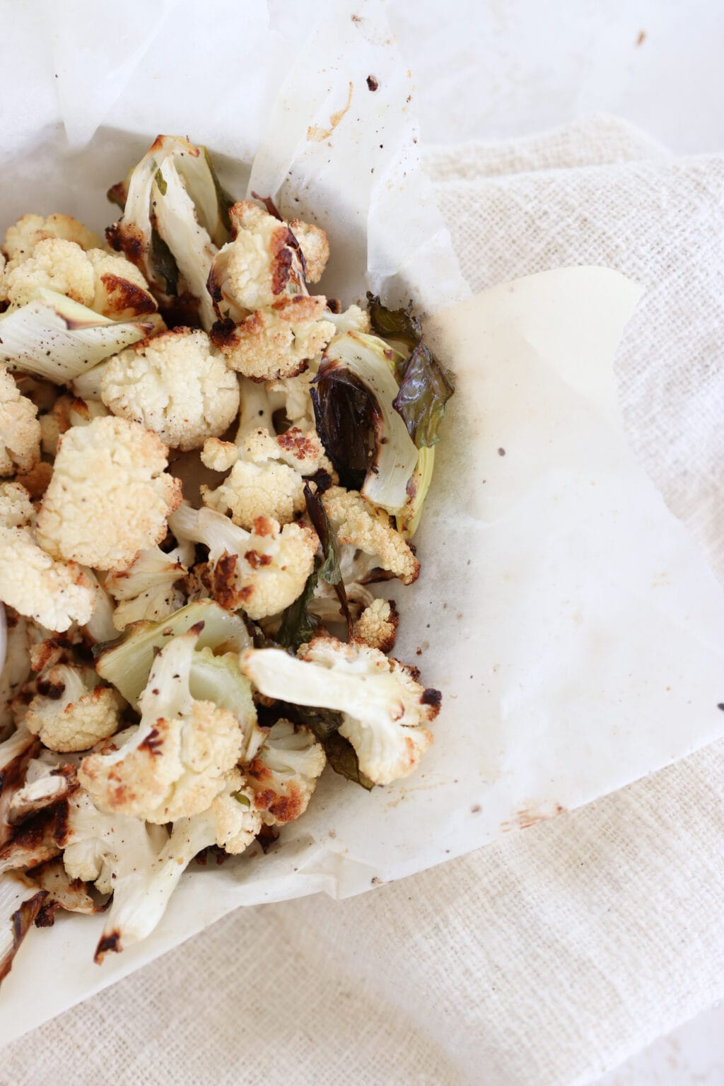 A zoomed in photo of roasted cauliflower in a parchment-lined bowl. It sits on a greyish white towel. 