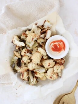 A parchment-lined bowl filled with roasted cauliflower and spicy yogurt.