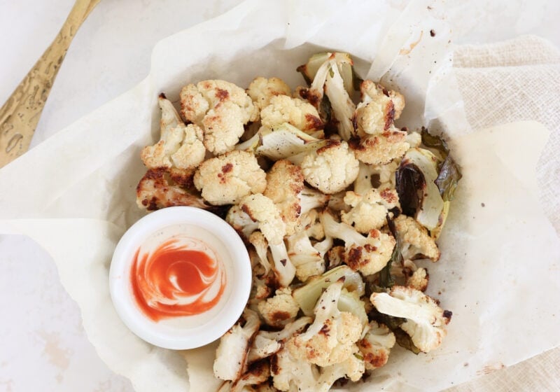 A parchment-lined bowl filled with roasted cauliflower and spicy yogurt.