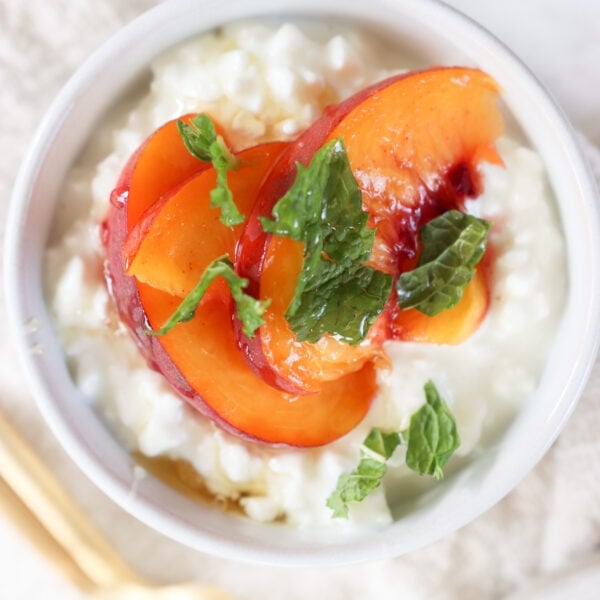 A bowl filled with cottage cheese and topped with fresh peach slices and mint.