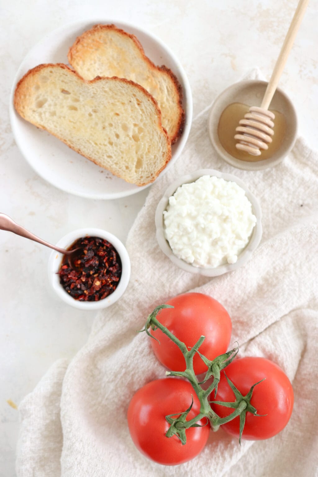 Ingredients for the recipe laid out include sourdough toast, honey, cottage cheese, chili crisp oil, and tomatoes