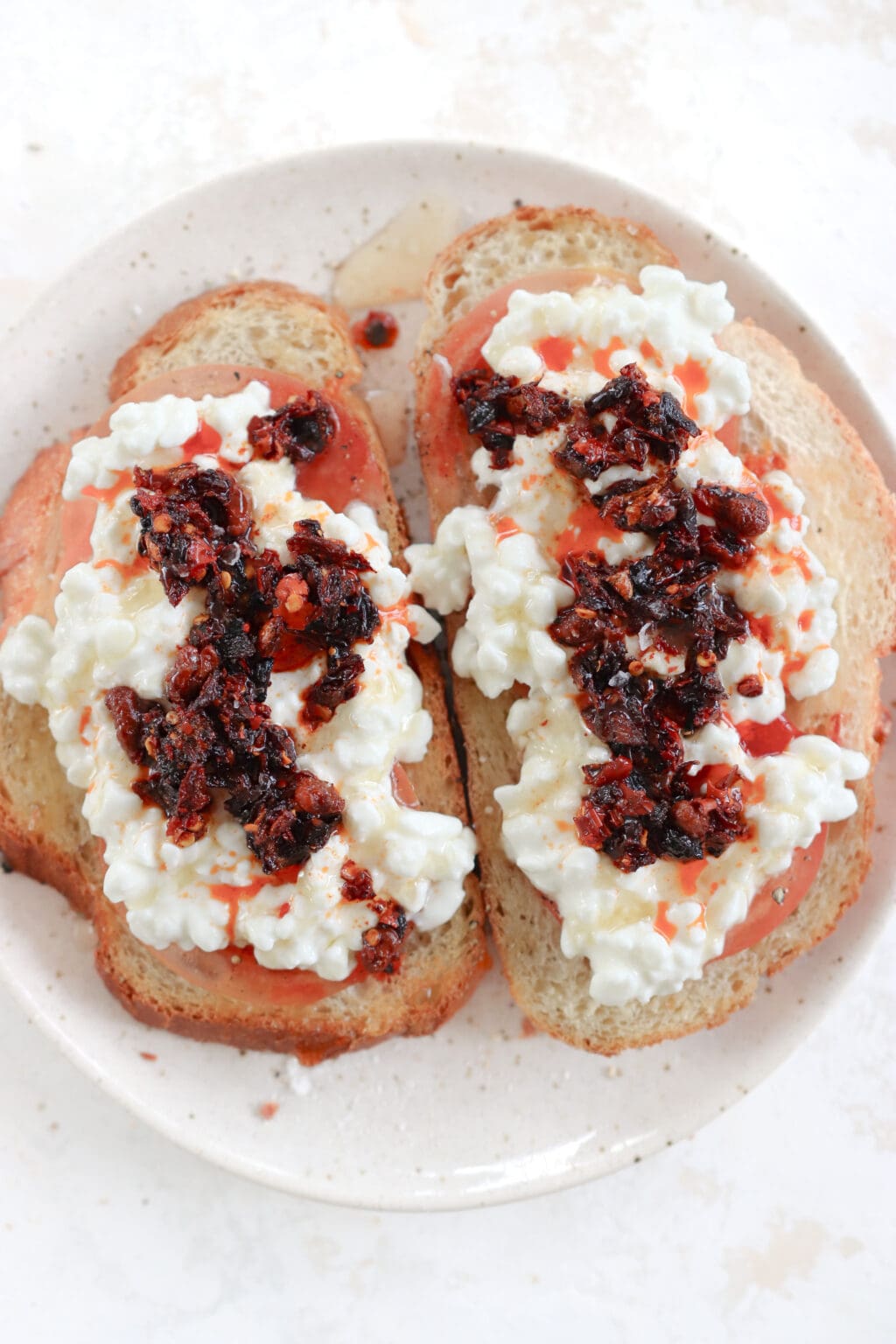 Two pieces of toast topped with tomato, cottage cheese, chili crisp oil and honey on a plate