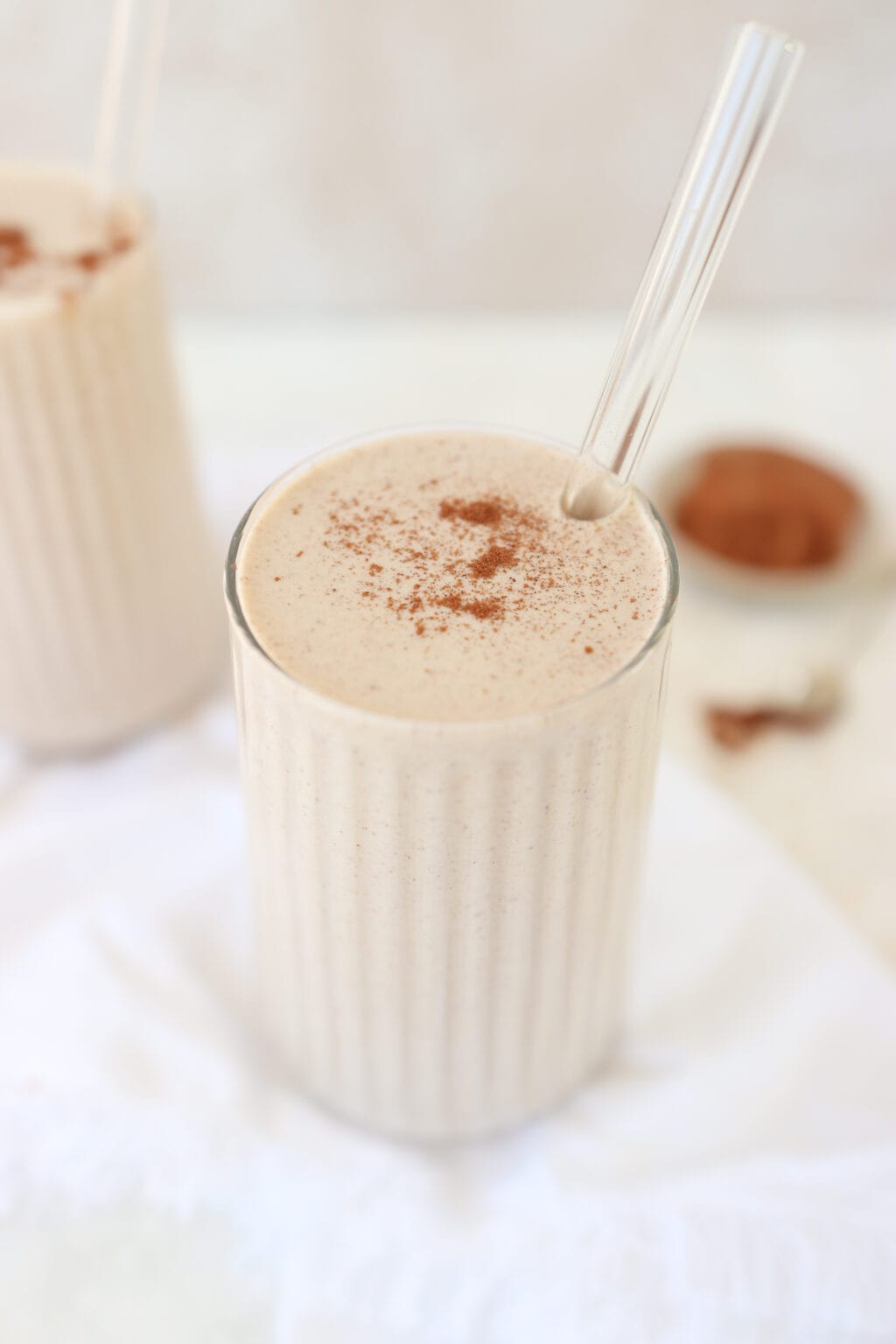 A cinnamon roll smoothie in a glass with a glass straw.