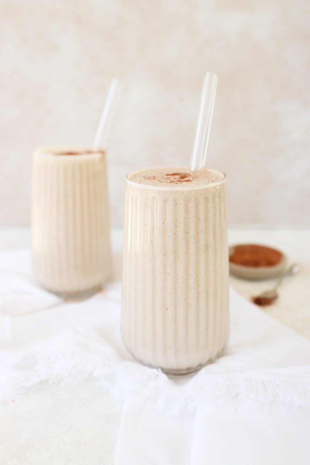 Two glasses of cinnamon roll smoothie with glass straws in them 