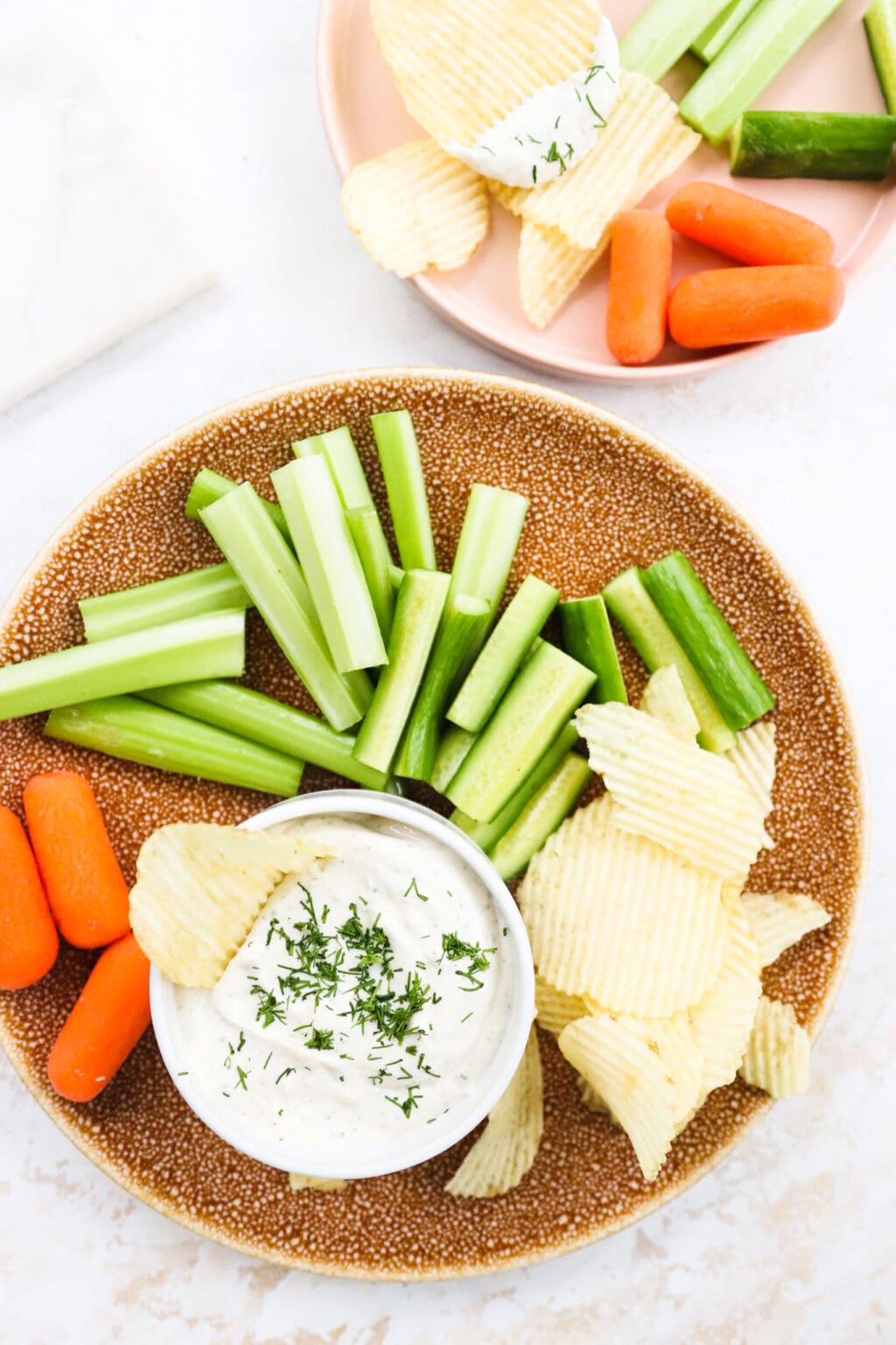 Celery, carrots, and ripple chips on a brown plate with a white bowl of french onion cottage cheese dip