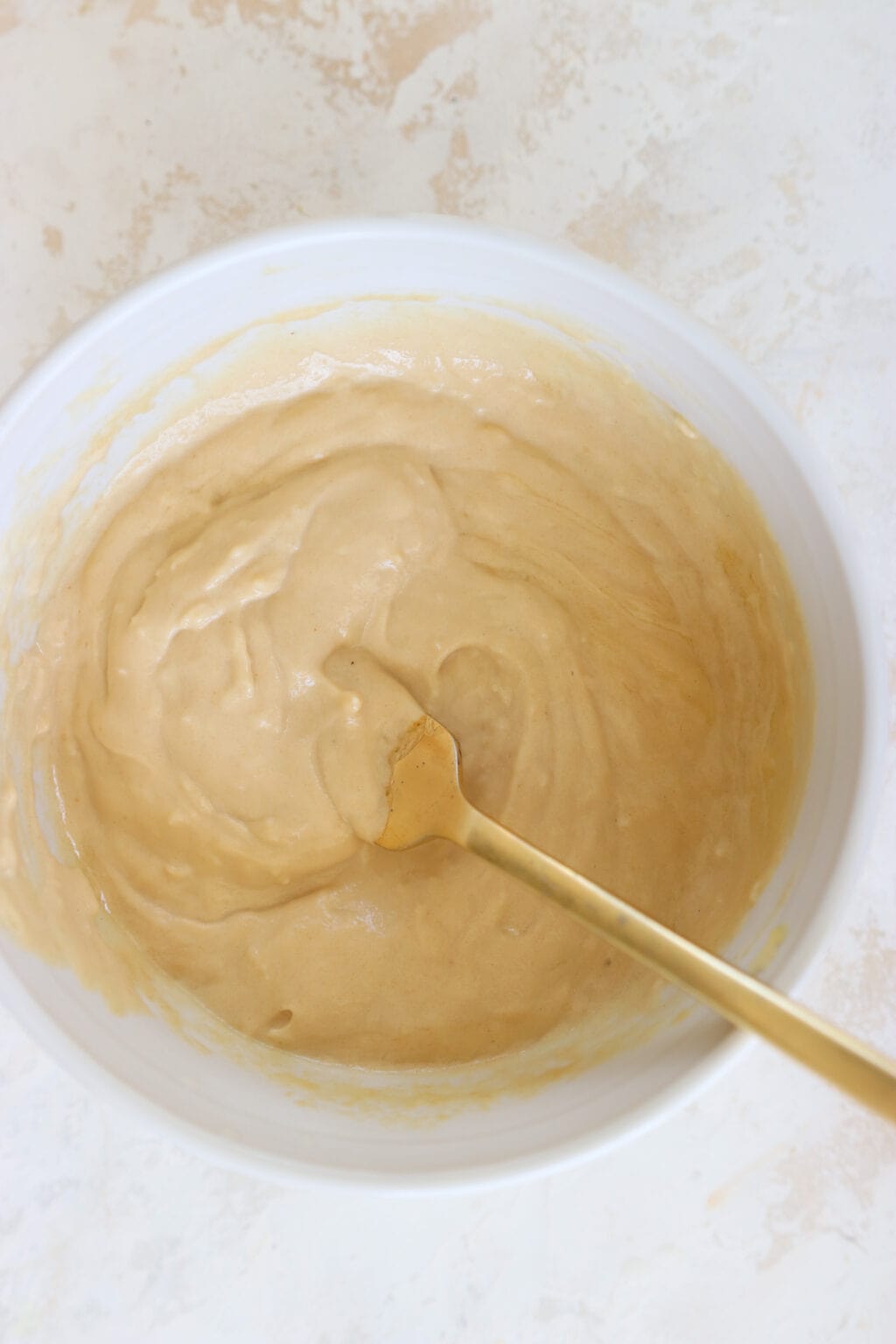 Lemon tahini sauce in a white bowl with a gold spoon