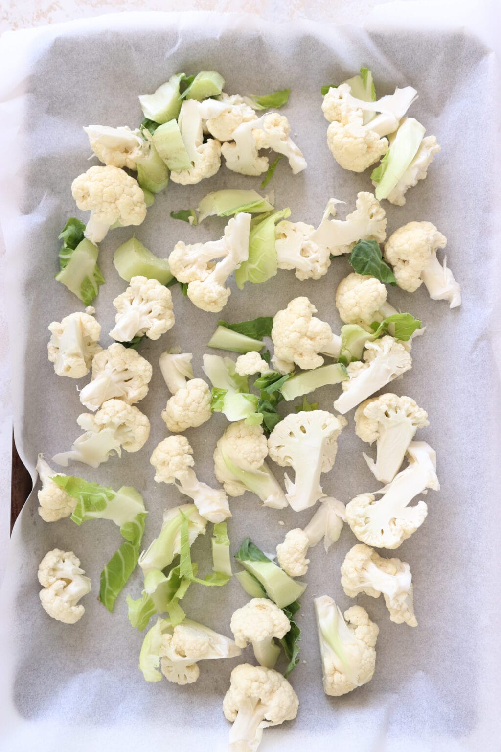 Cauliflower florets cut into pieces and laid out on a baking sheet which is lined with parchment paper