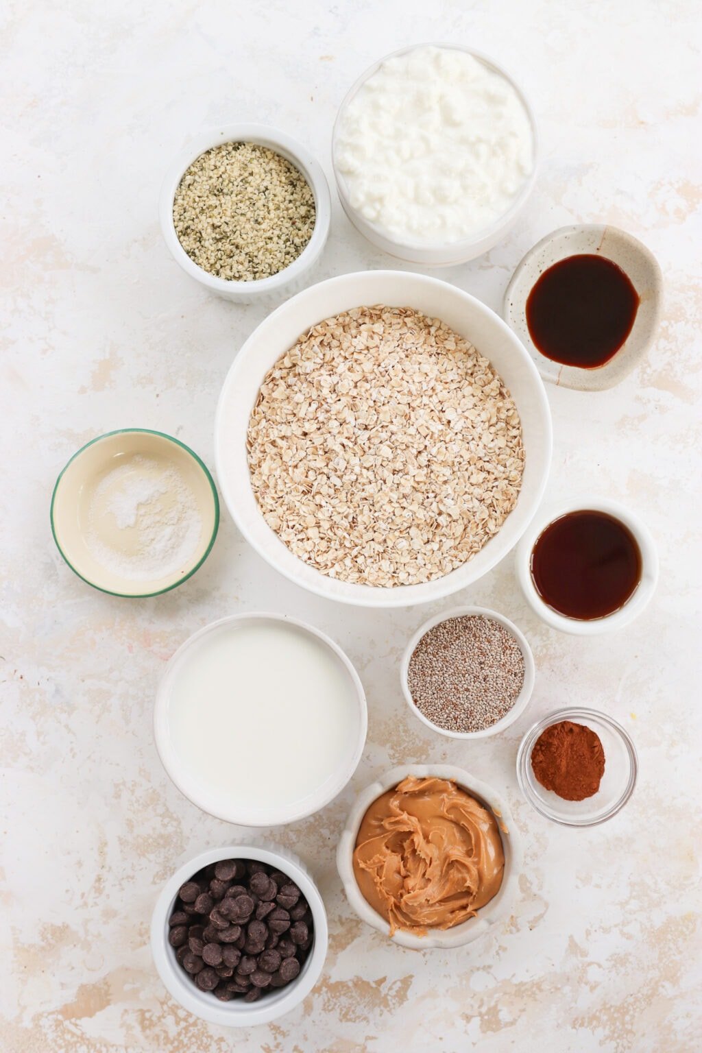 Ingredients for High Protein Cottage Cheese Blended Overnight Oats in white and glass bowls. Ingredients include quick oats, hemp hearts, chia seeds, vanilla extract, cinnamon, cottage cheese, peanut butter, milk and maple syrup.