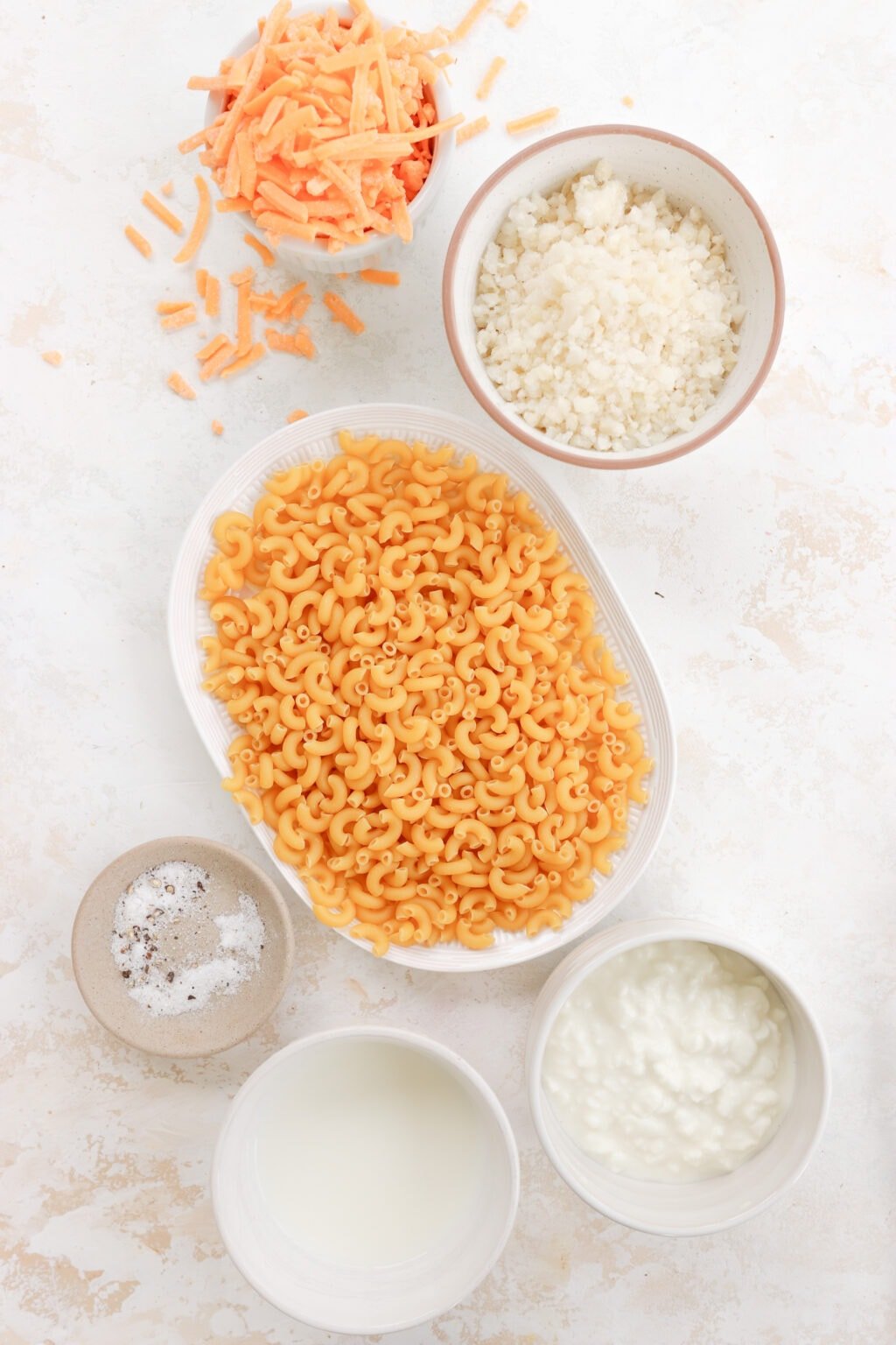 Ingredients for Creamy Cottage Cheese Mac and Cheese in white bowls, including elbow pasta, cottage cheese, milk, shredded cheddar cheese, garlic salt and cornstarch
