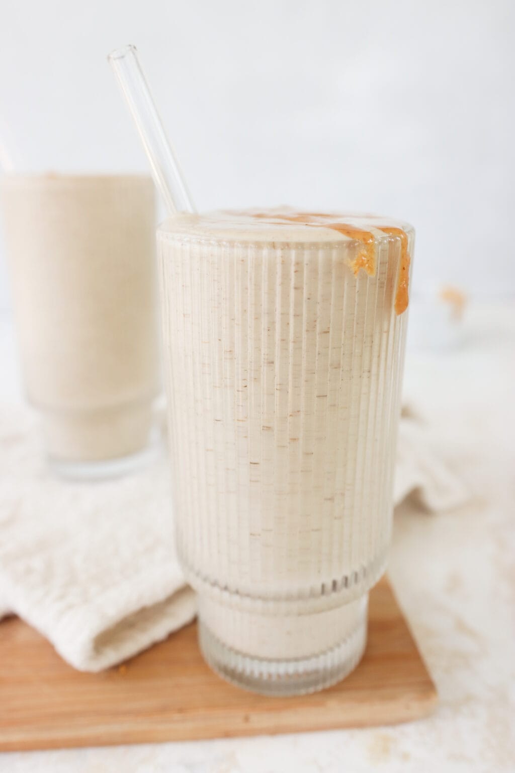 Two glasses filled with healthy peanut butter banana smoothie with a bowl of melted peanut butter on the side