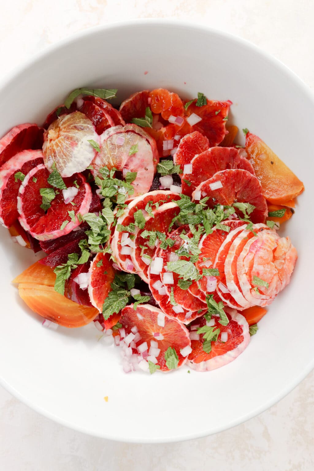 Ingredients for blood orange and roasted beet salad in a white bowl, including blood oranges, roasted beets, and mint