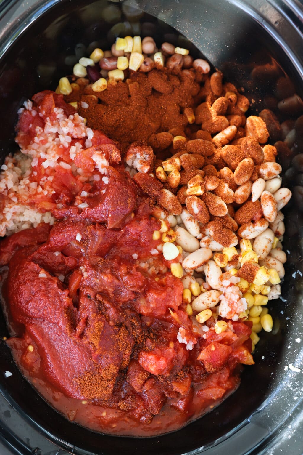 Ingredients in a slow cooker for a slow cooker sweet potato and turkey chili, including ground turkey, roasted sweet potatoes, onions, corn, garlic, mushrooms, tomatoes and cauliflower rice.