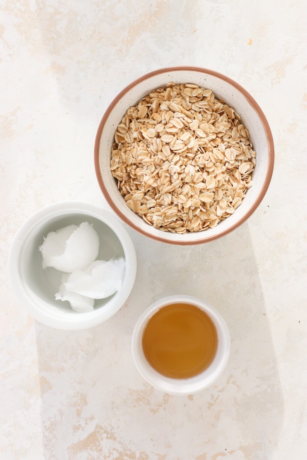 Ingredients for 3-Ingredient Gluten Free Cheesecake Crust in white bowls, including oats, coconut oil, and honey