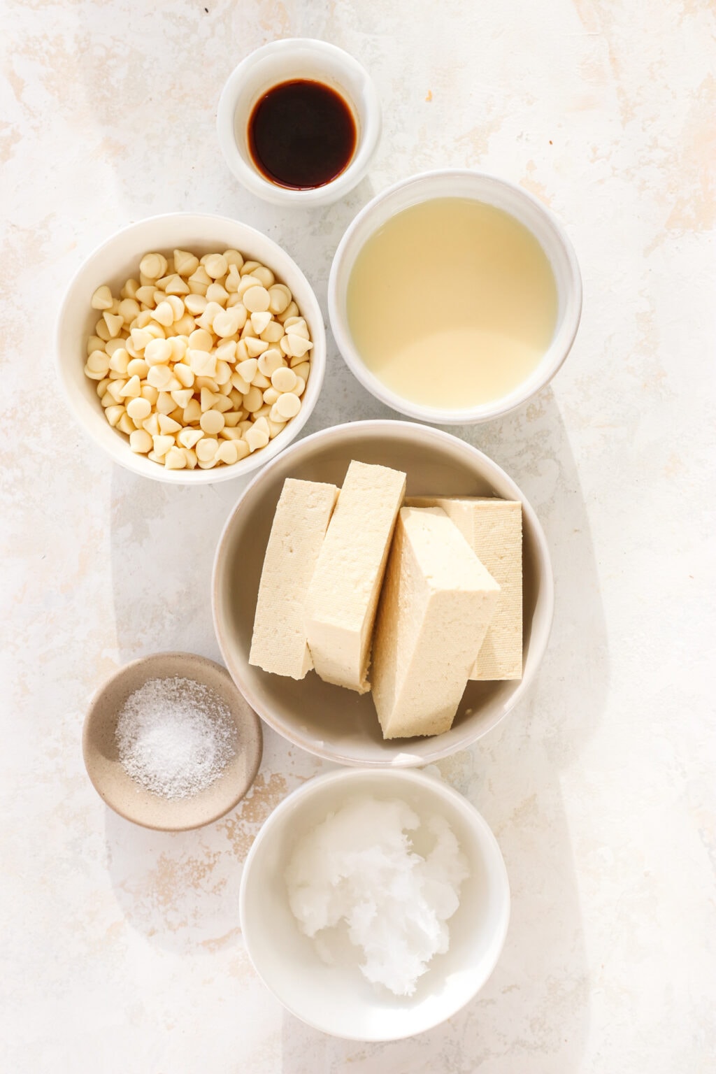 Ingredients for a 5 ingredient tofu eggnog mini creamy cheesecake, including tofu, white chocolate, eggnog, vanilla, coconut oil, and salt