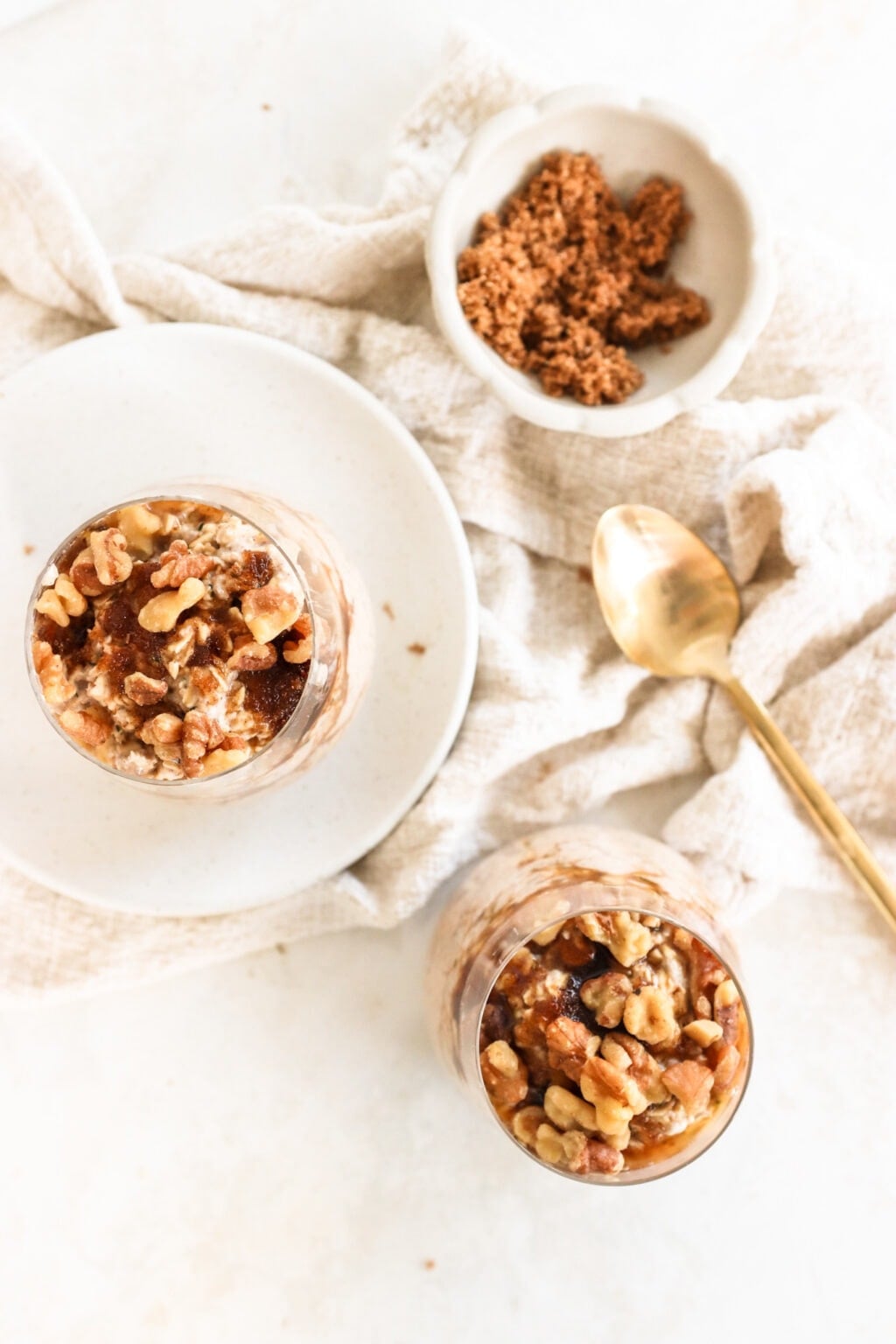 Brown sugar and Greek yogurt overnight oats in three glass bowls on top of a soft, cream-colored tablecloth with a gold spoon