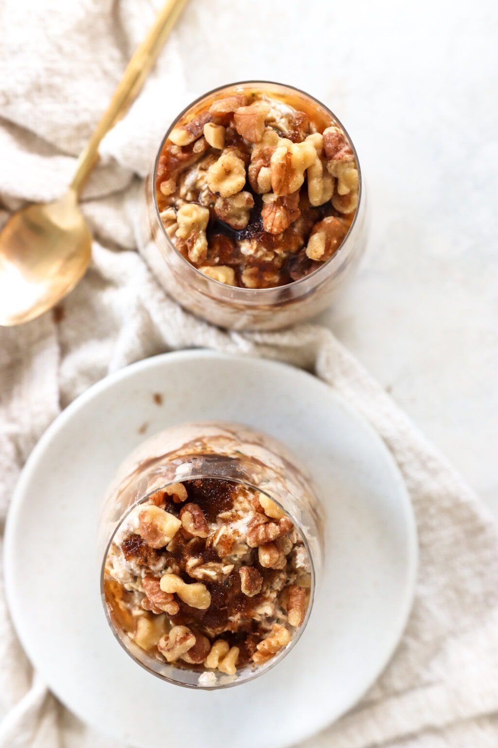 Brown sugar and Greek yogurt overnight oats in two glass bowls on top of a soft, cream-colored tablecloth with a gold spoon
