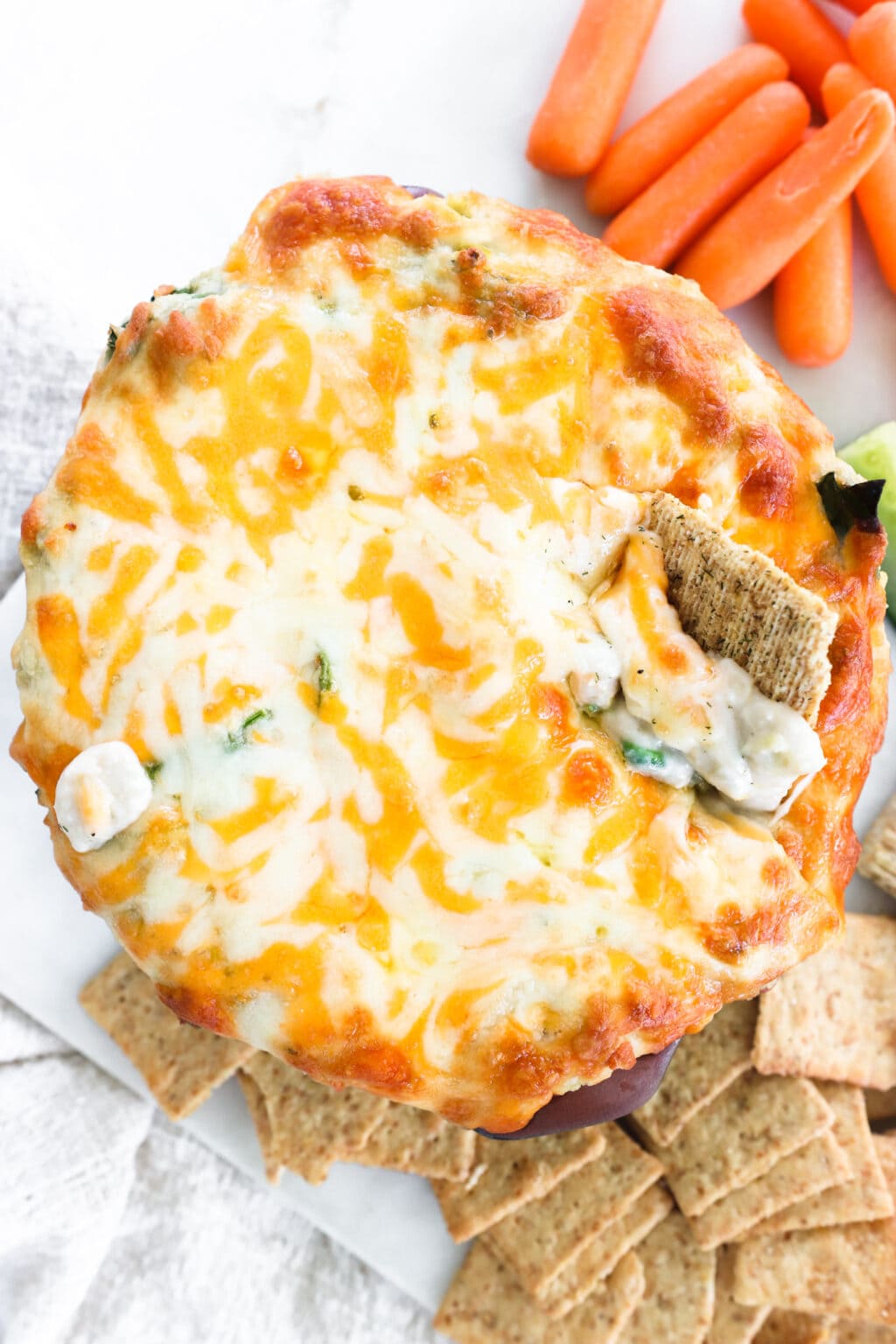 A dish of healthy white bean, spinach and artichoke dip on a white platter with crackers and carrots for dipping