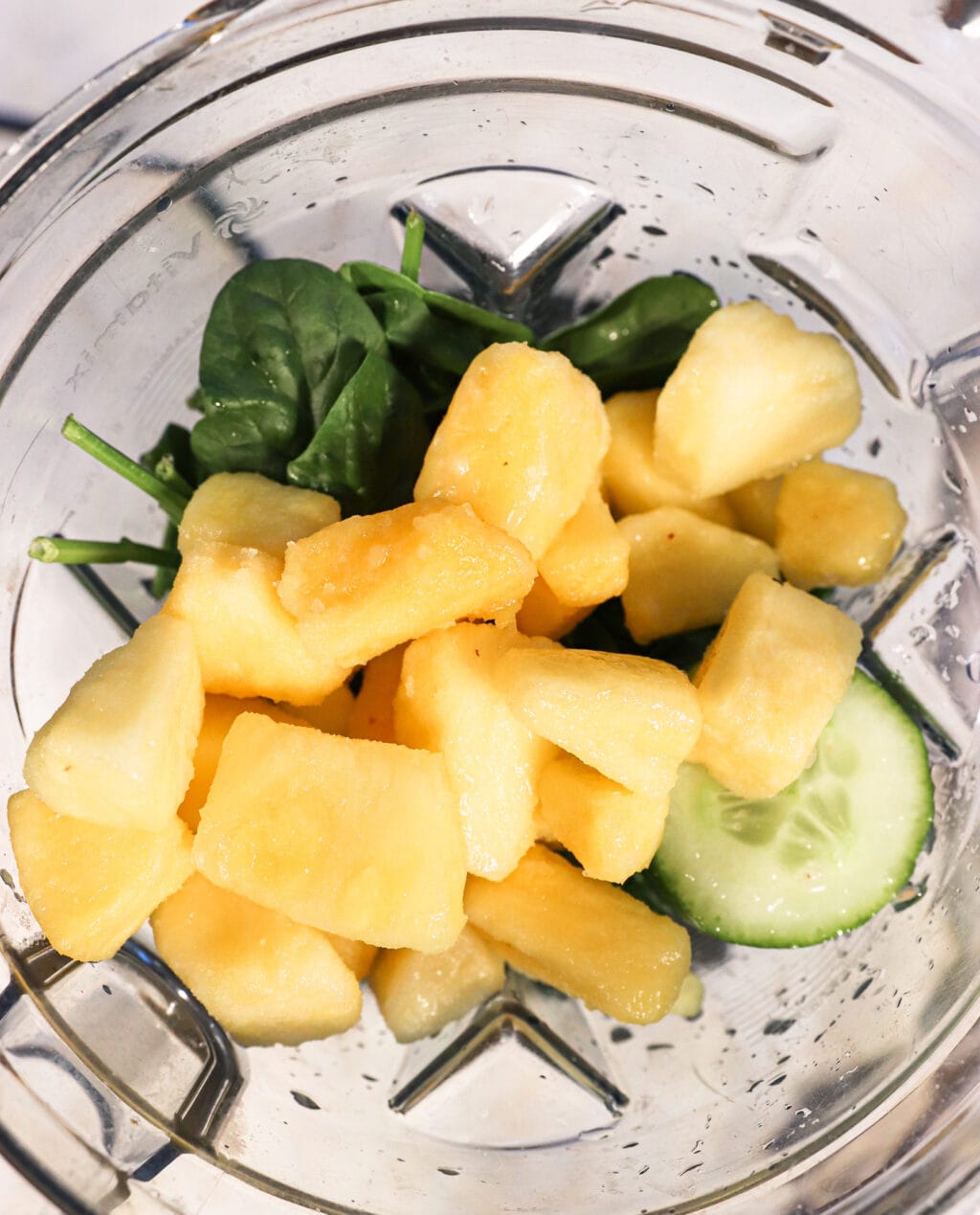 Ingredients for Blender Juice With Spinach, Pineapple & Cucumber, including lemon juice, cucumber, spinach, pineapple, and water in a blender.