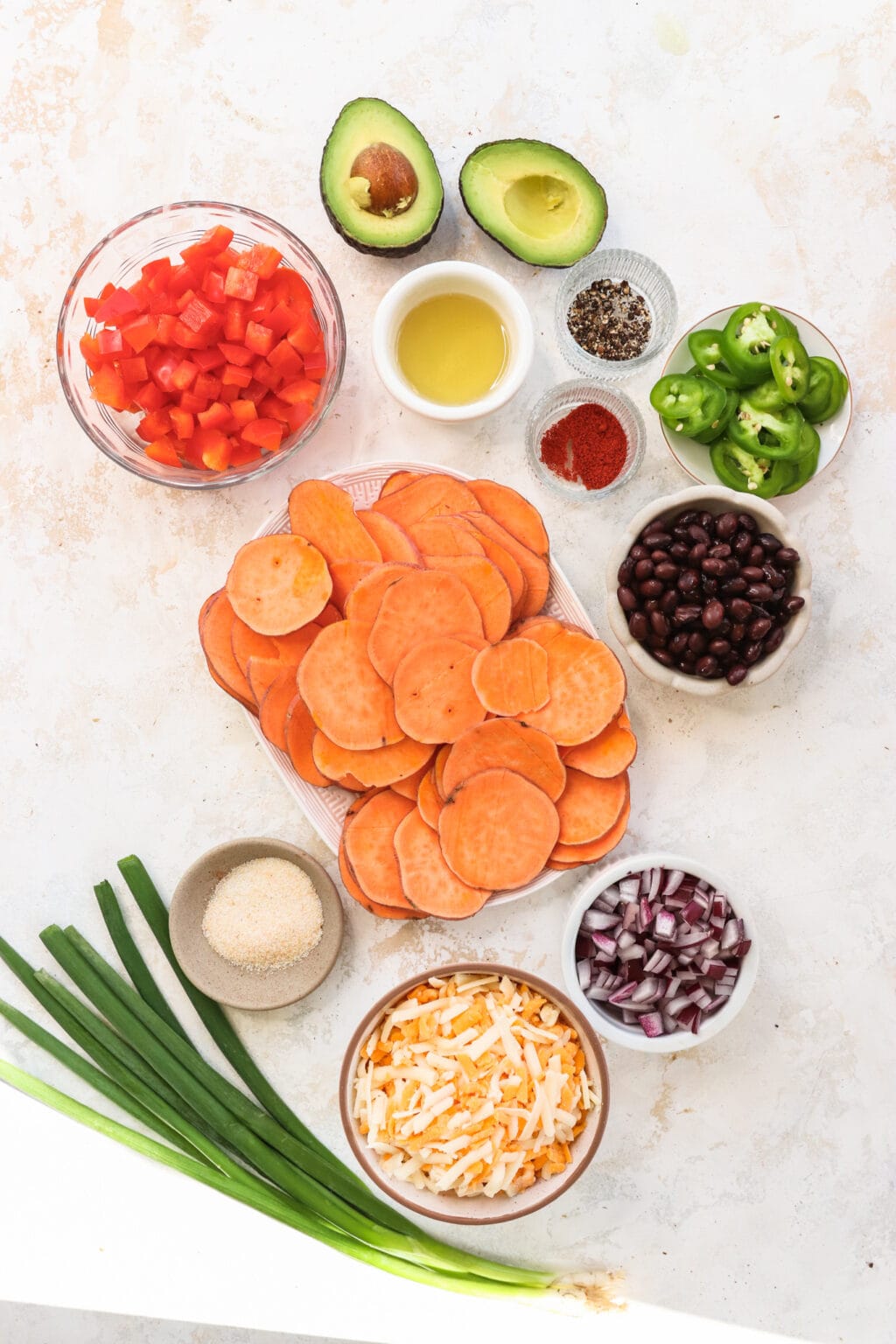 Ingredients for Healthy Black Bean & Bell Pepper Sweet Potato Nachos, including sweet potatoes, avocado oil, pepper, paprika, garlic salt, nacho cheese blend, black beans, bell peppers, red onion, jalapeno, green onion, avocado, sour cream, salsa