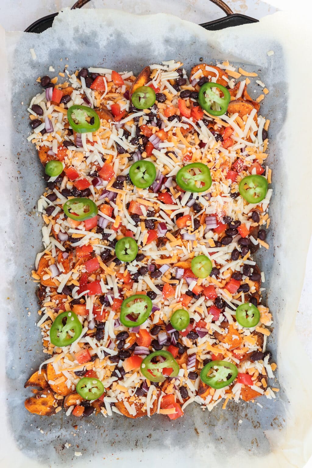Healthy Black Bean & Bell Pepper Sweet Potato Nachos on a baking sheet with parchment paper