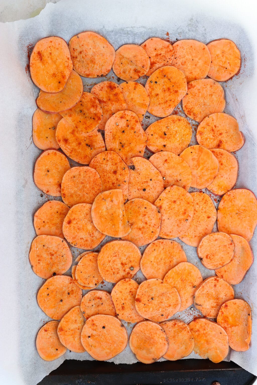 Uncooked sweet potato chips on a baking sheet with parchment paper