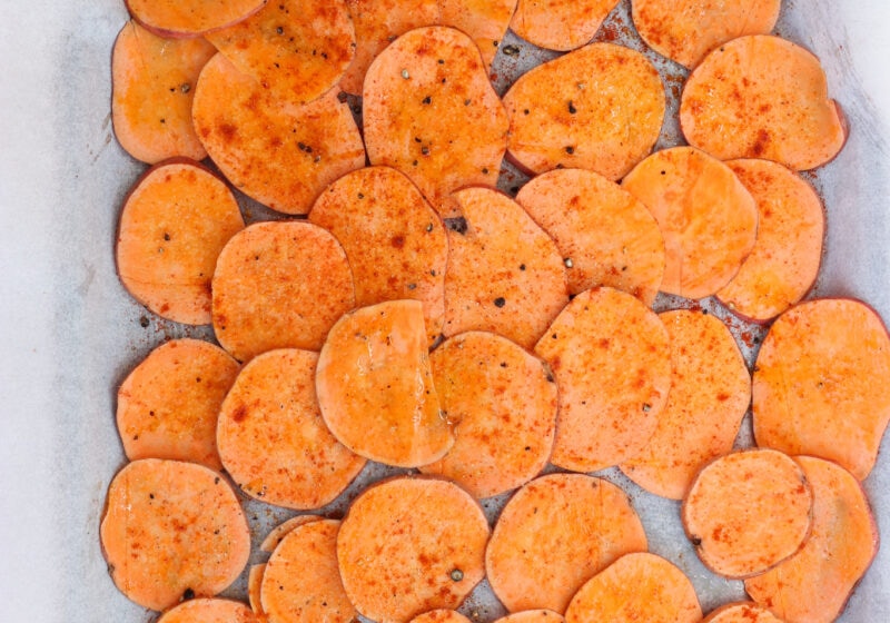 Uncooked sweet potato chips on a baking sheet with parchment paper