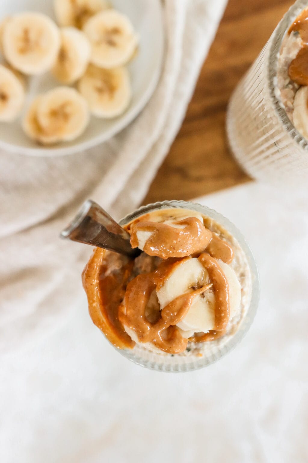 Peanut Butter & Banana Kefir Overnight Oats in two glass cups on a wood cutting board with sliced banana on the side