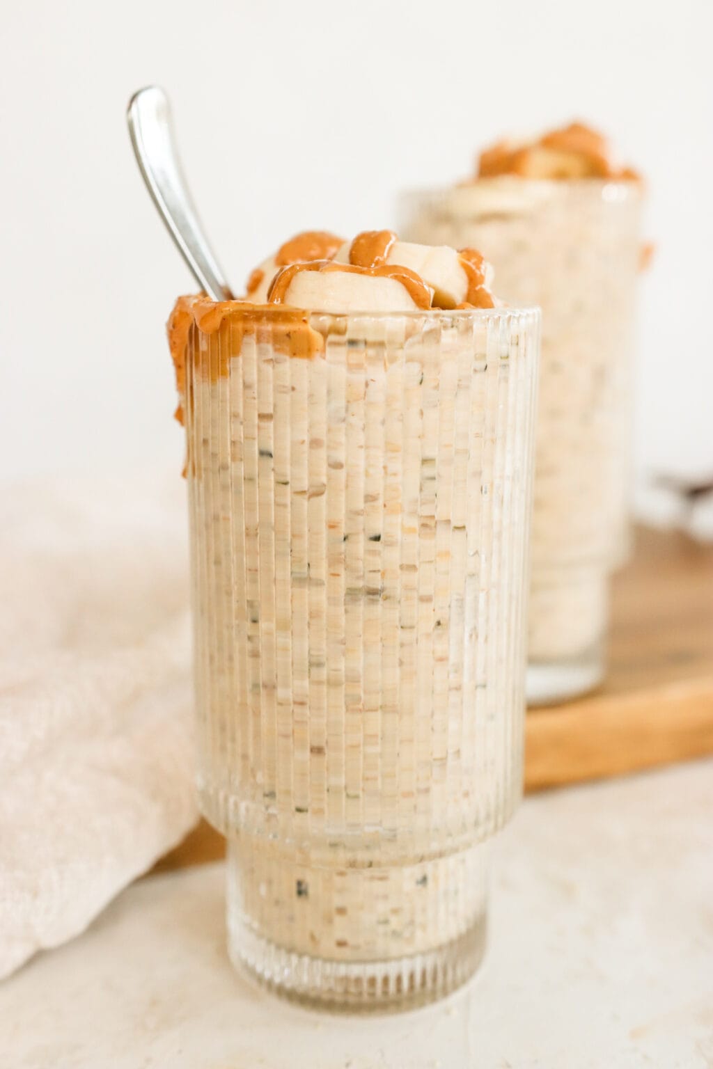 Peanut Butter & Banana Kefir Overnight Oats in two glass cups on a wood cutting board