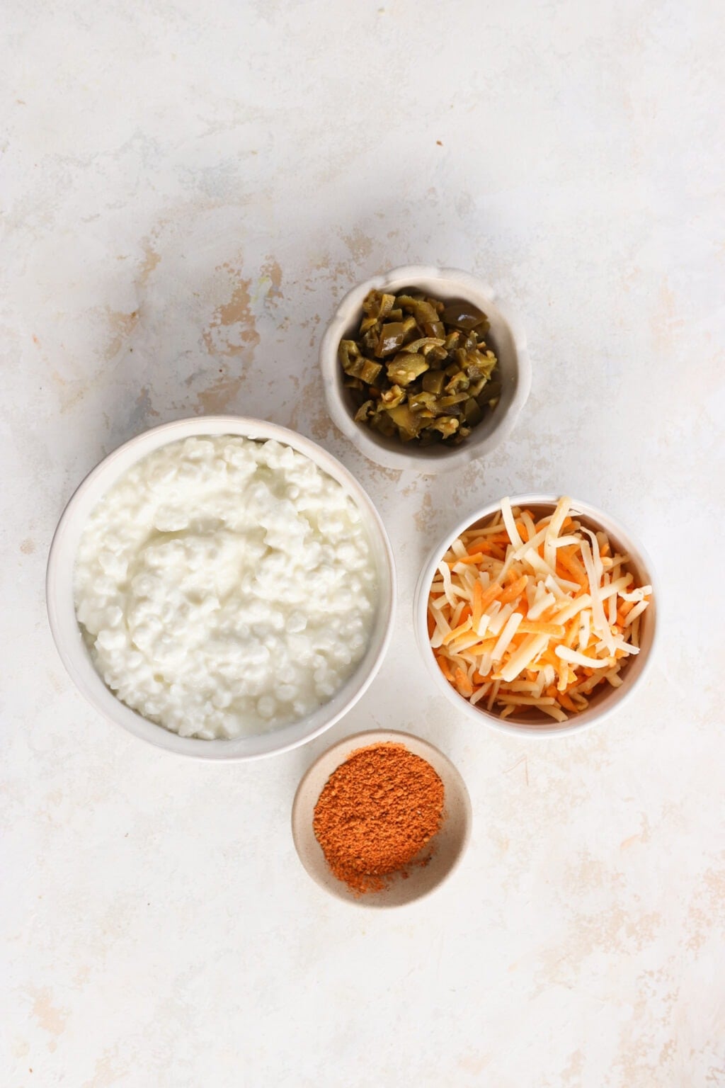 Ingredients for 5-Minute Warm Queso Dip With Cottage Cheese in white bowls, including, cottage cheese, shredded tex mex cheese, taco seasoning, pickled jalapenos