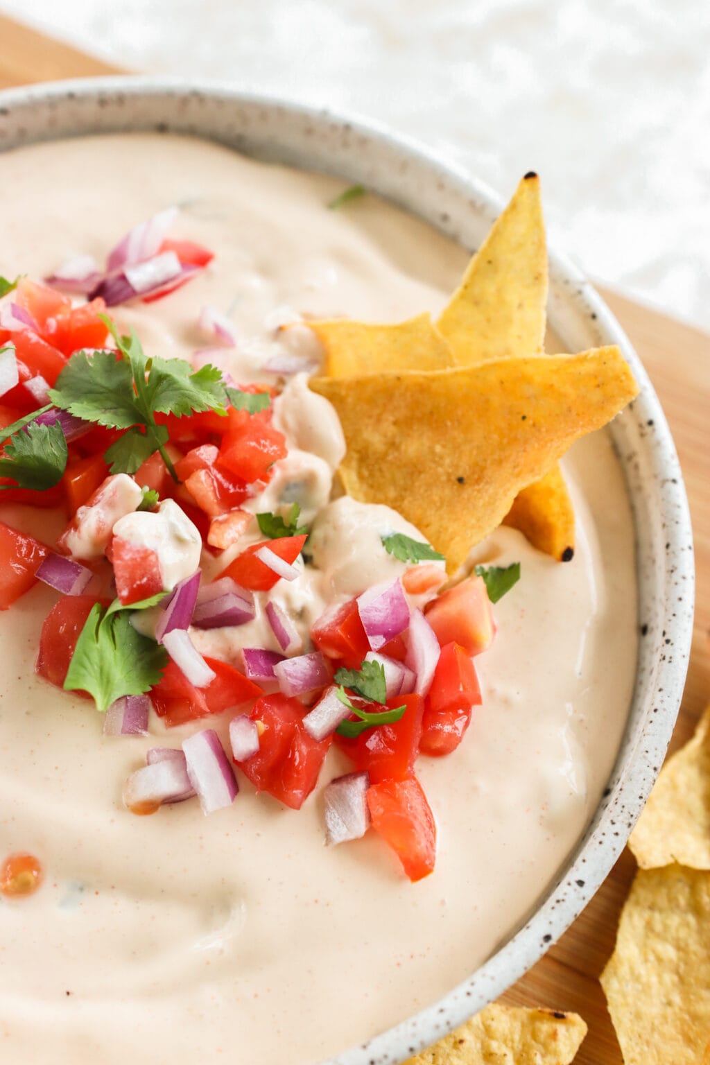 5-Minute Warm Queso Dip With Cottage Cheese in a white bowl with a tortilla chip dipped into it