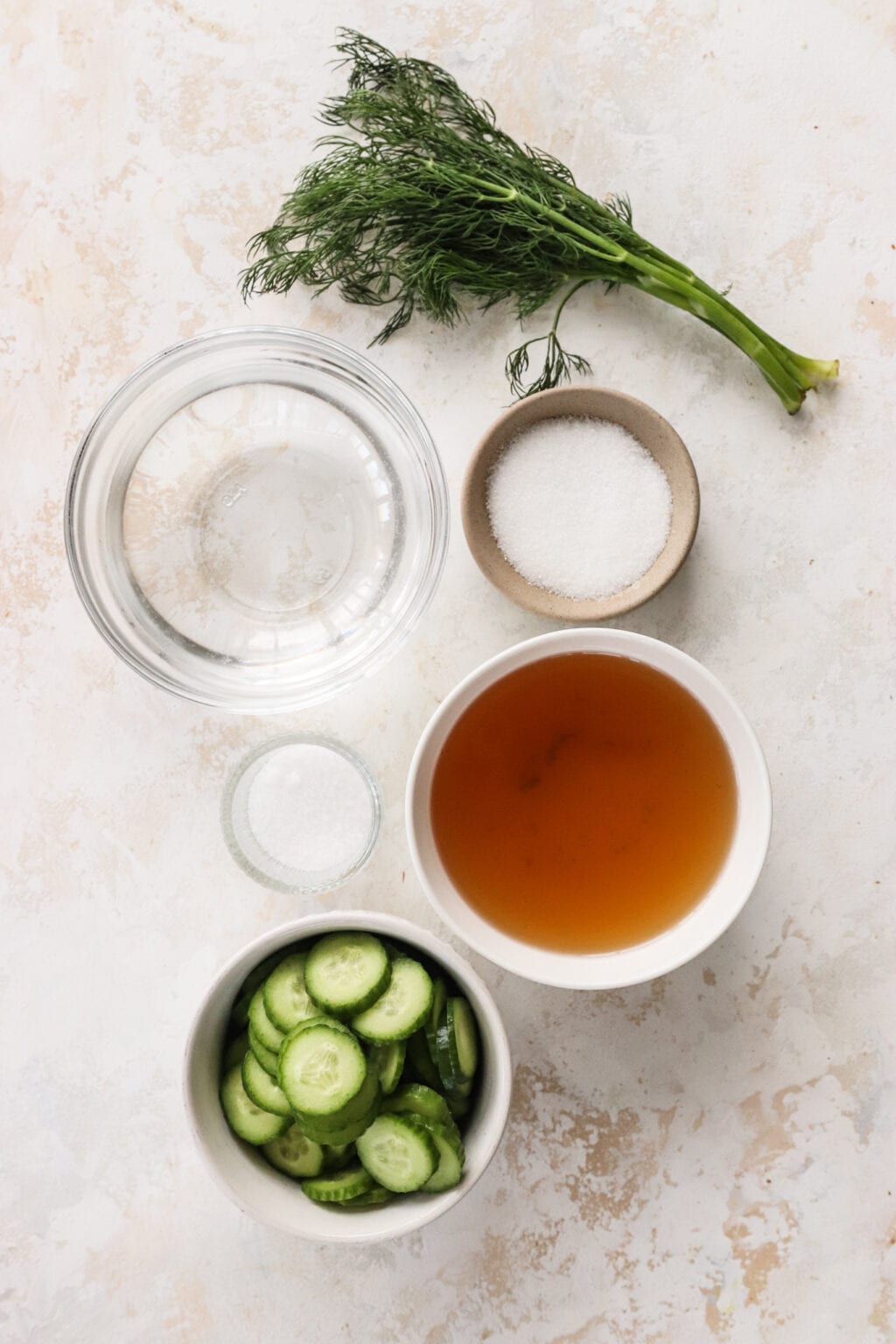 Ingredients for Apple Cider Vinegar Cucumber Pickles with Dill in small bowls, including cucumbers, hot water, apple cider vinegar or white vinegar, salt, sugar, fresh dill