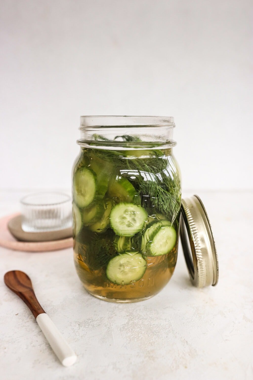 Apple Cider Vinegar Cucumber Pickles with Dill in a pickle jar with a wooden spoon and glass bowl beside the jar