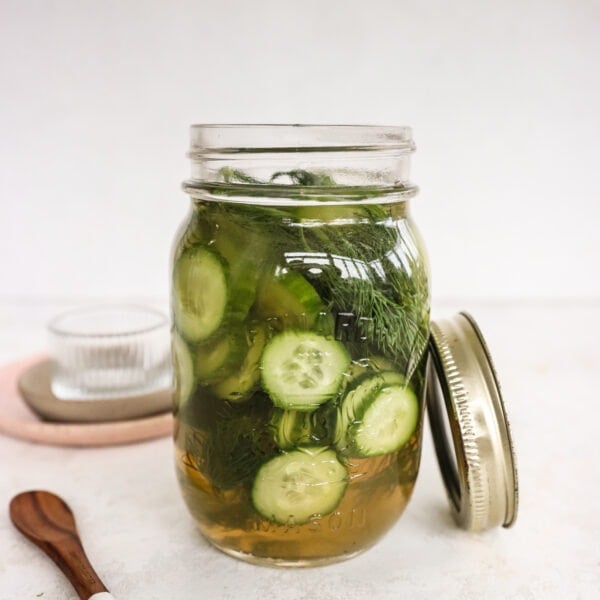 Apple Cider Vinegar Cucumber Pickles with Dill in a pickle jar with a wooden spoon and glass bowl beside the jar