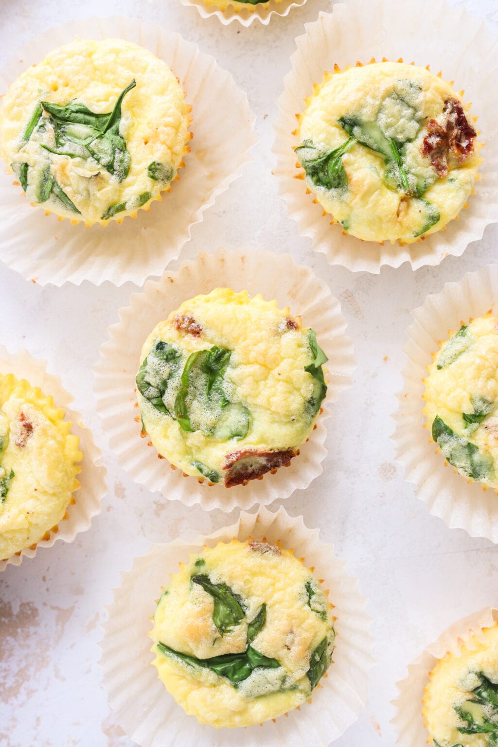 Egg Bites with Cottage Cheese, Spinach & Sun-dried Tomatoes on a table in parchment paper baking cups