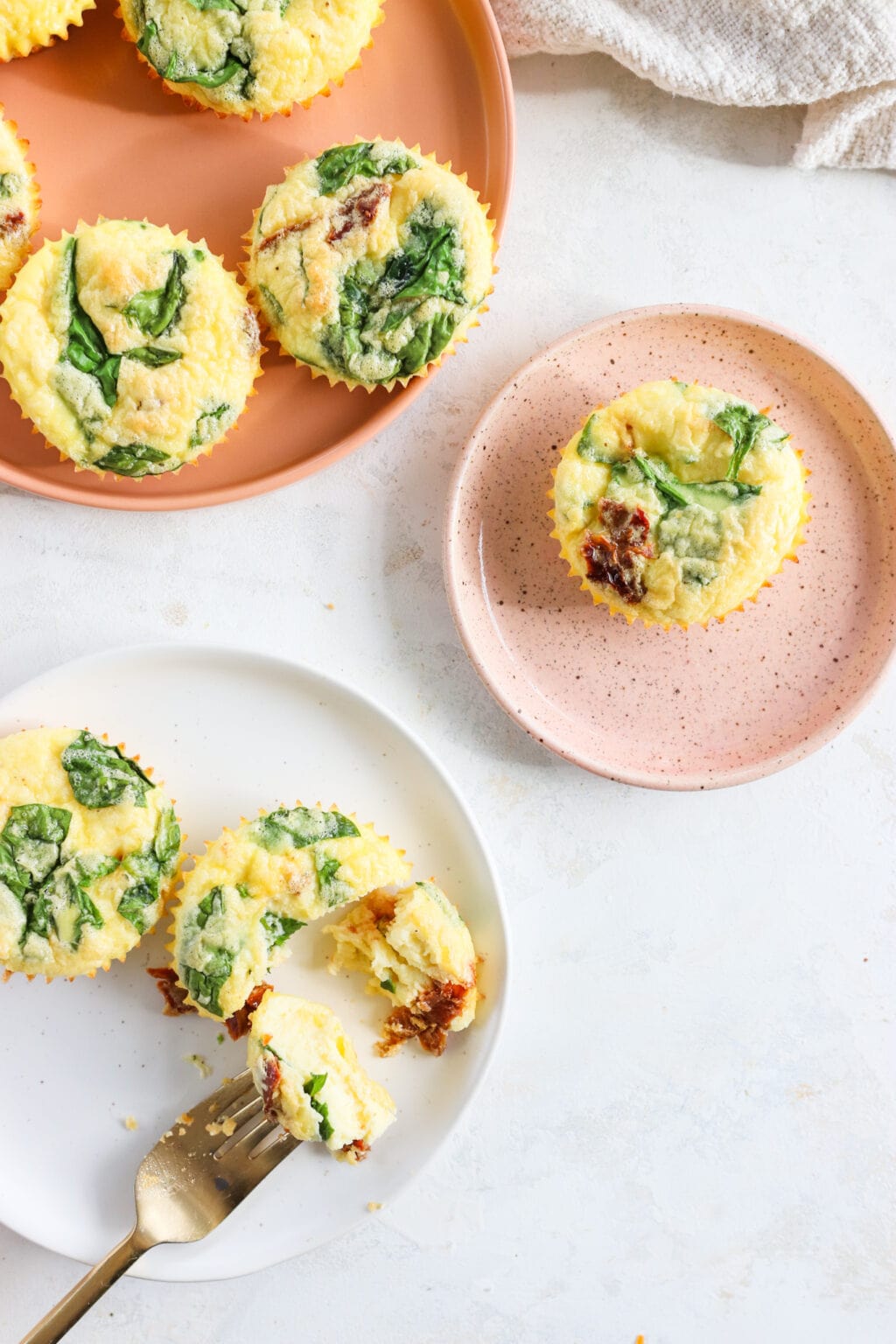 Egg Bites with Cottage Cheese, Spinach & Sun-dried Tomatoes on two pink plates and one white plate