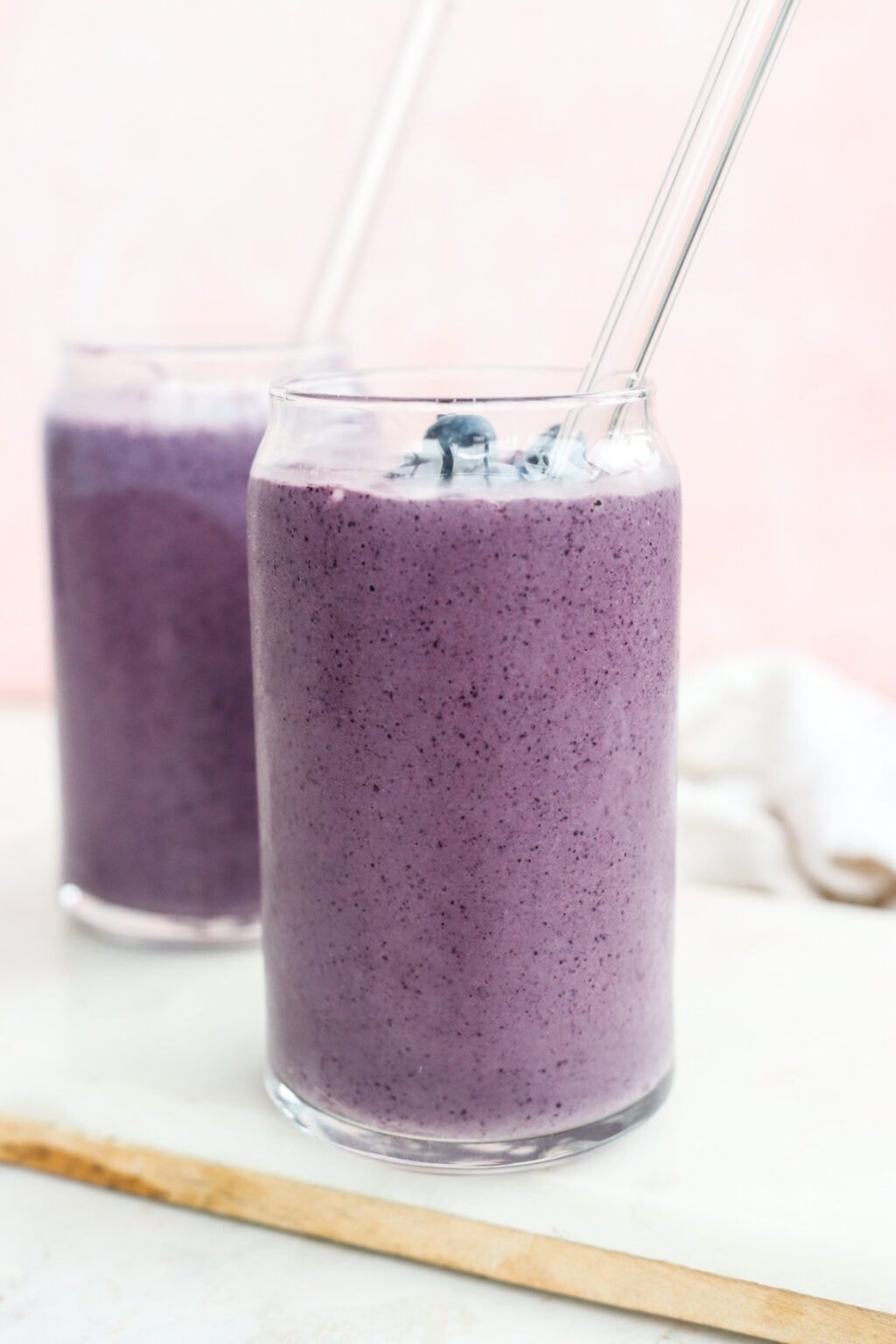 Two clear glasses filled with High Protein Blueberry Breakfast Smoothie with Cottage Cheese on a cutting board