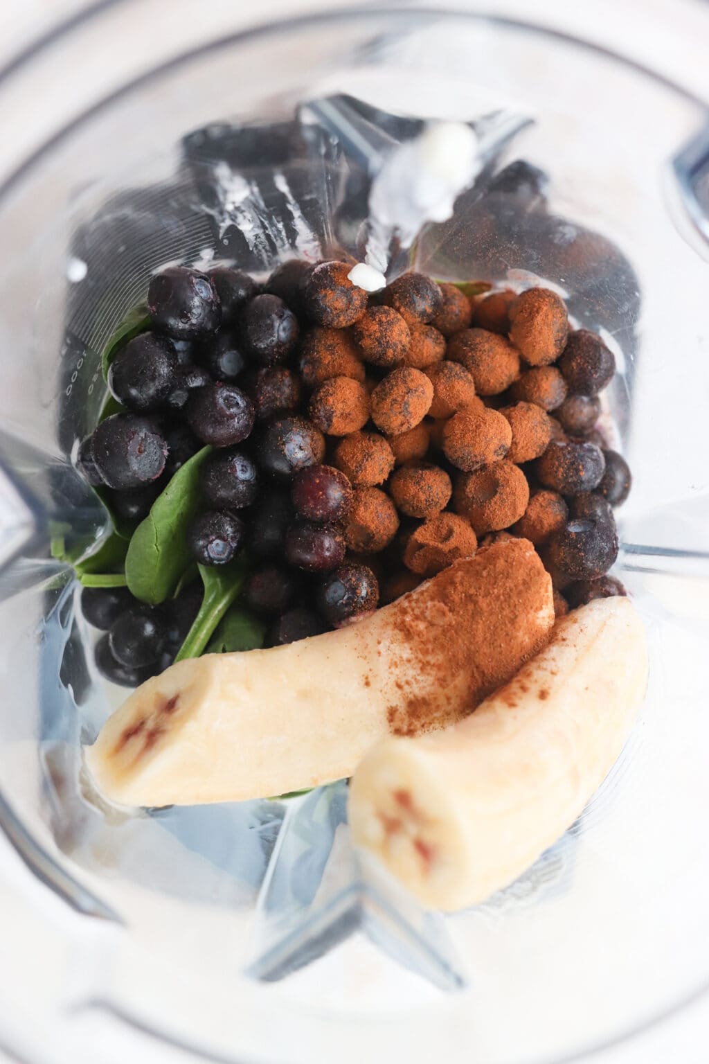 Ingredients for High Protein Blueberry Breakfast Smoothie in a blender, including blueberries, banana, cottage cheese, milk, cinnamon, spinach, chia seeds, hemp hearts