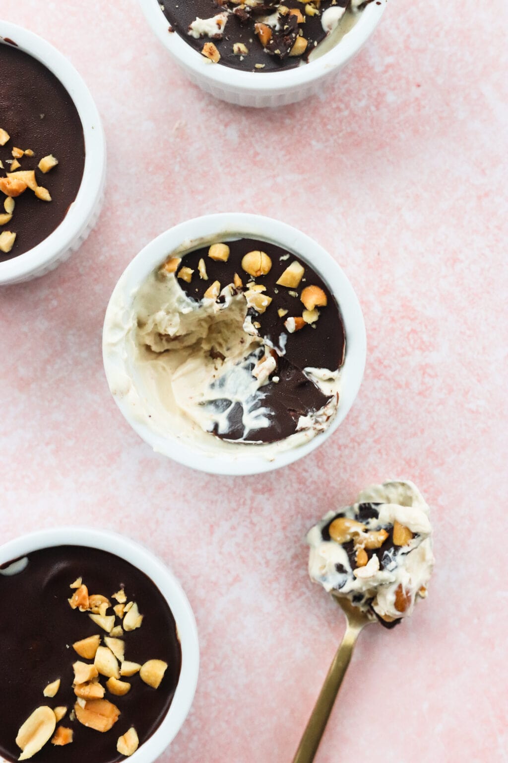 Peanut Butter & Greek Yogurt Cups with Magic Chocolate Shell in white bowls on a pink marble countertop white a scoop taken out of the middle bowl