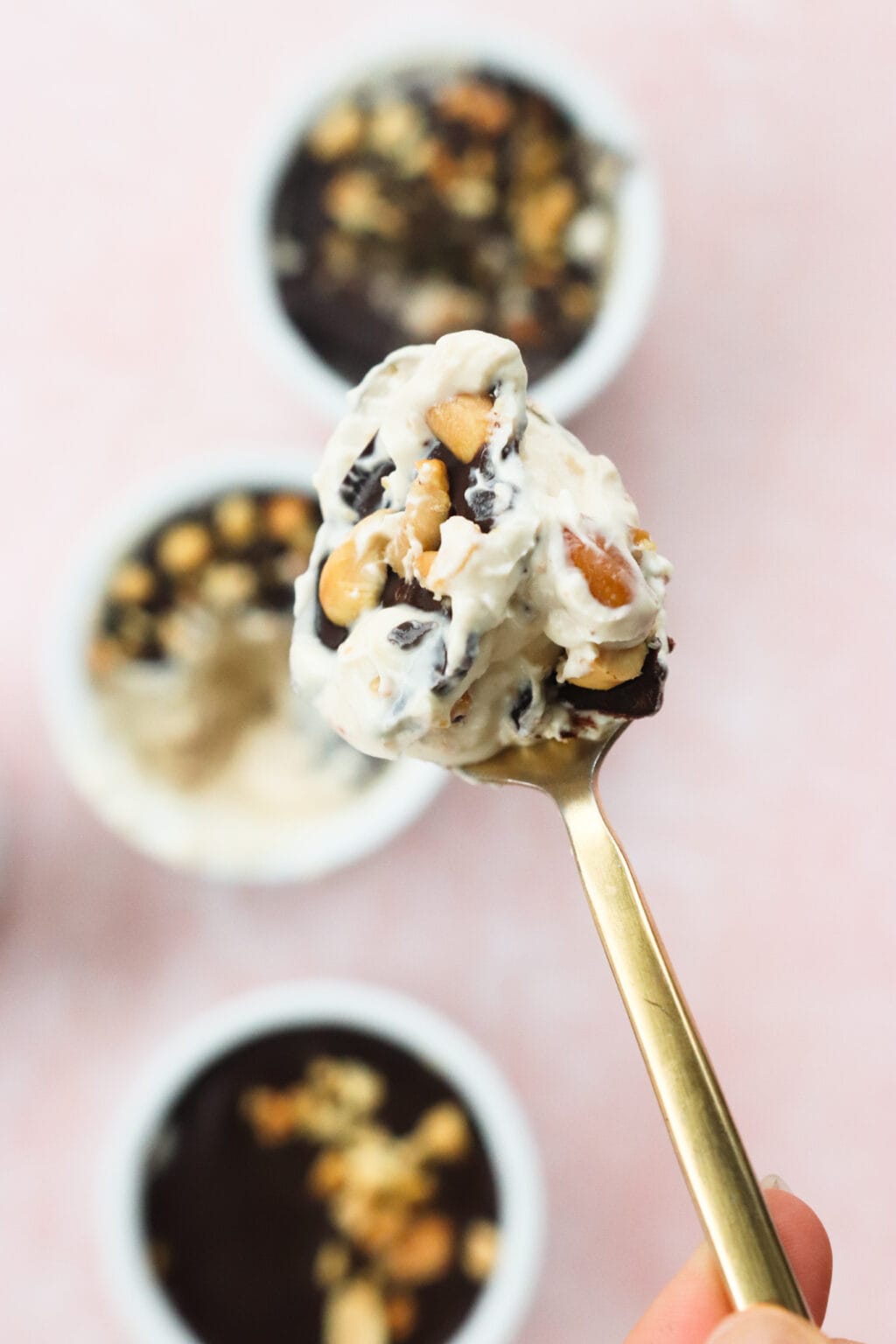 A spoonful of Peanut Butter & Greek Yogurt Cups with Magic Chocolate Shell on a gold spoon with three bowls in the background