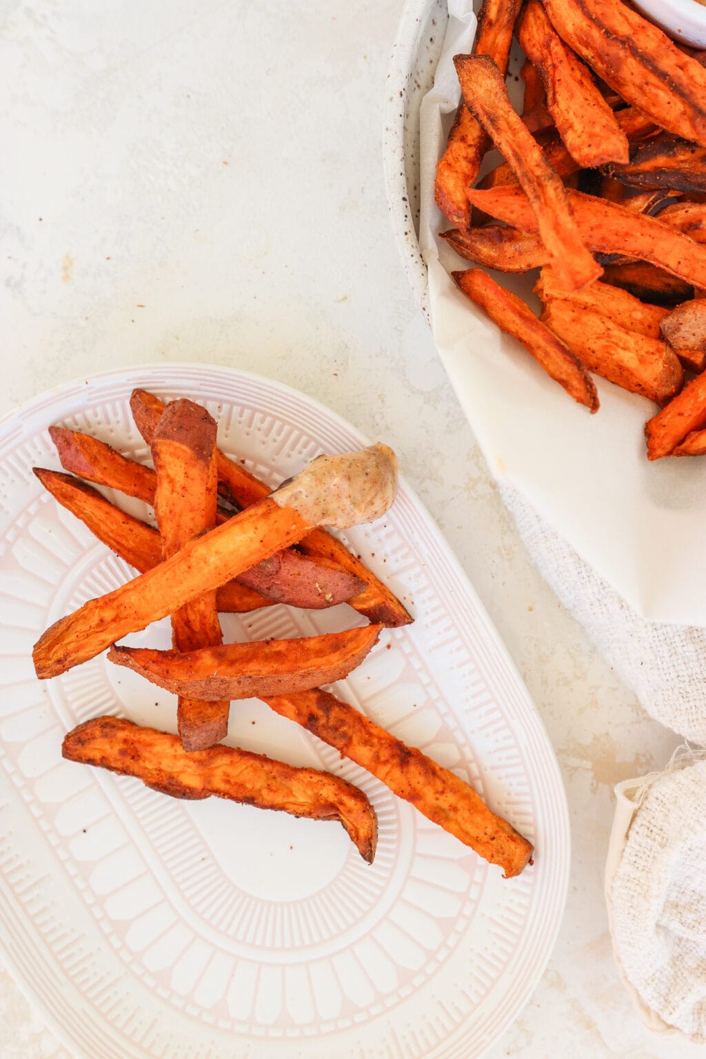 4 Ingredient Crispy Air Fryer Sweet Potato Wedges in a white bowl with a few fries on a white plate beside it
