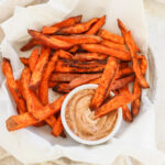 4 Ingredient Crispy Air Fryer Sweet Potato Wedges in a white bowl with parchment paper and dip on the side