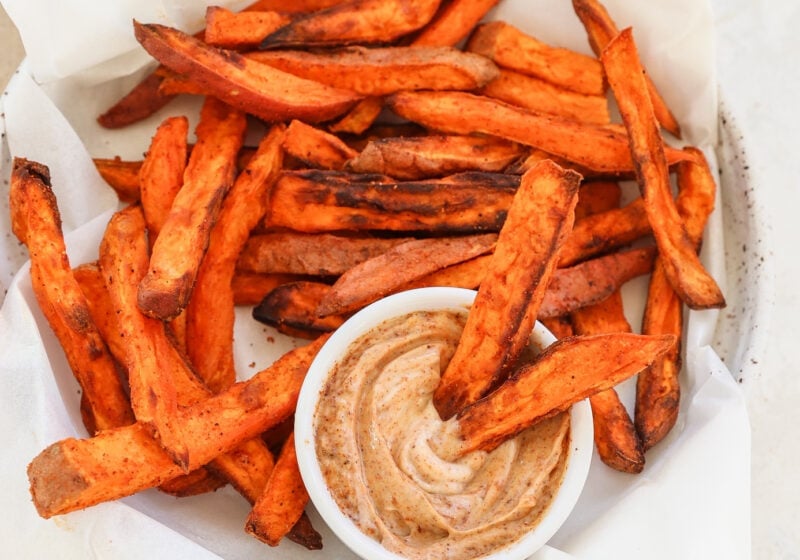 4 Ingredient Crispy Air Fryer Sweet Potato Wedges in a white bowl with parchment paper and dip on the side