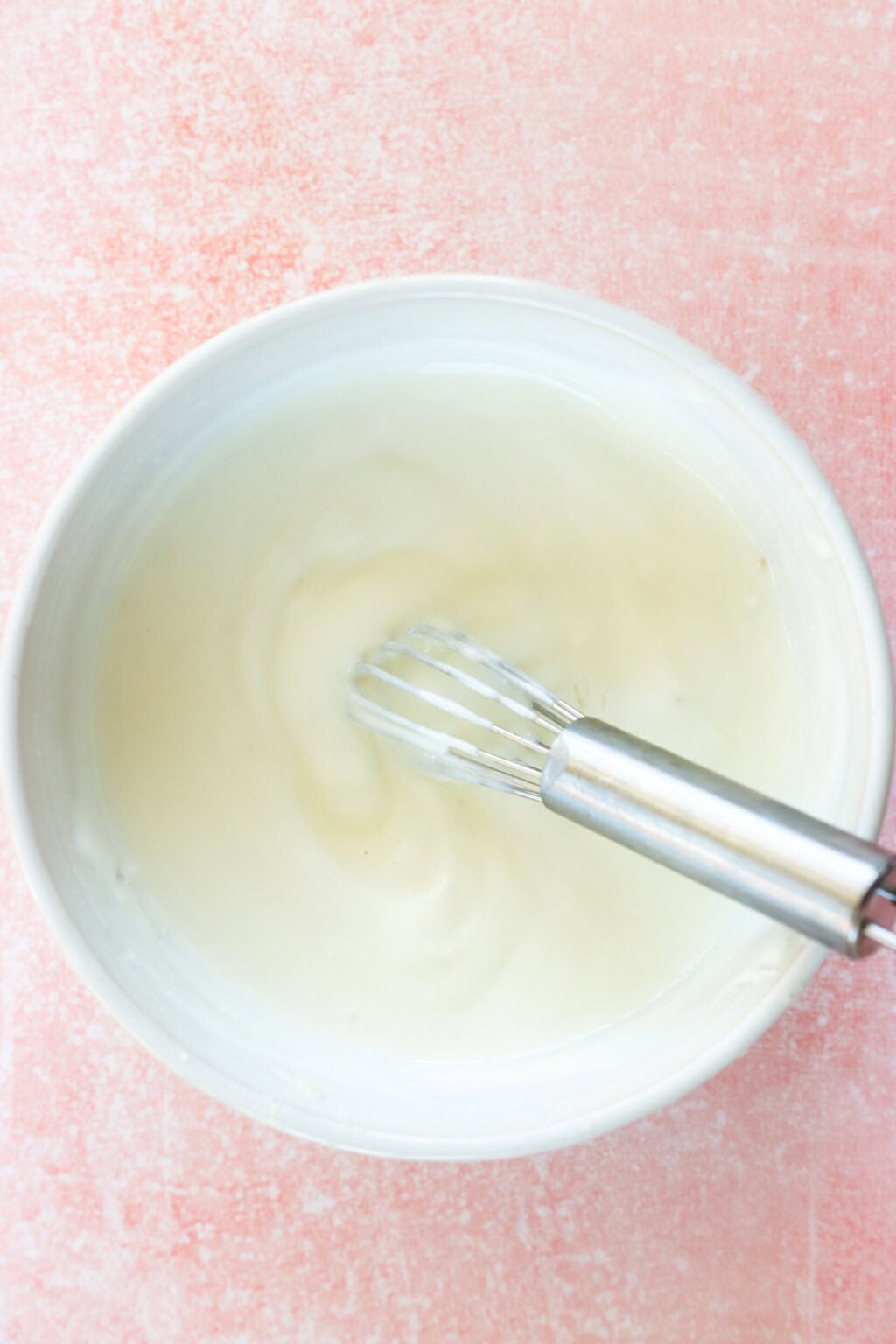 Ingredients for 4 Ingredient Greek Yogurt Lime Crema in a white bowl with a metal whisk on a pink countertop